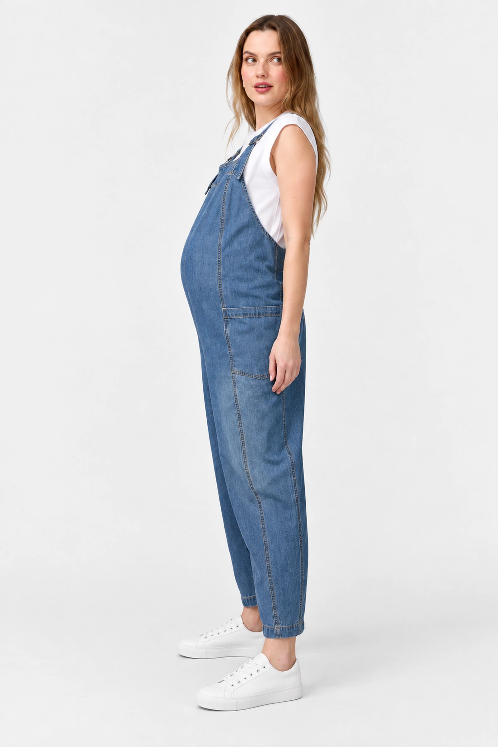 Side view of Ingrid & Isabel Everyday Denim Maternity Overalls in medium wash on a pregnant model.