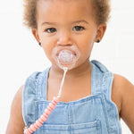Baby with pacifier attached to clothes via pink silicone bead pacifier clip