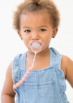 Baby with pacifier attached to clothes via pink silicone bead pacifier clip
