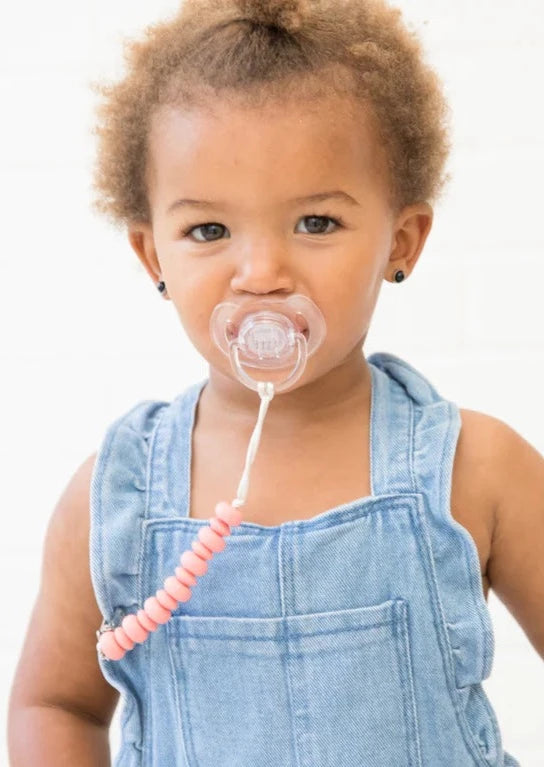 Baby with pacifier attached to clothes via pink silicone bead pacifier clip